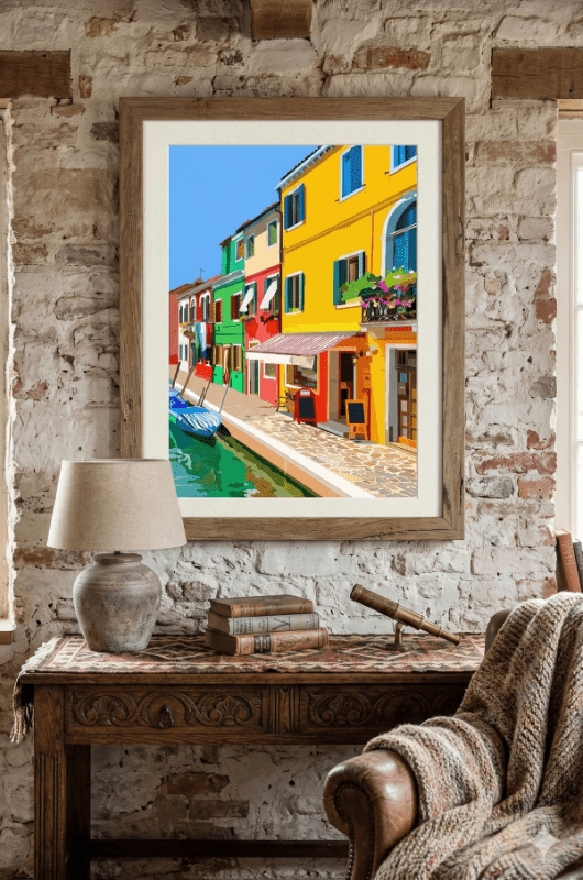 Framed artwork of colorful buildings in a canal scene on a brick wall above a wooden table.