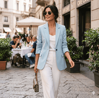 Woman in light blue blazer and white pants walking on a city street.